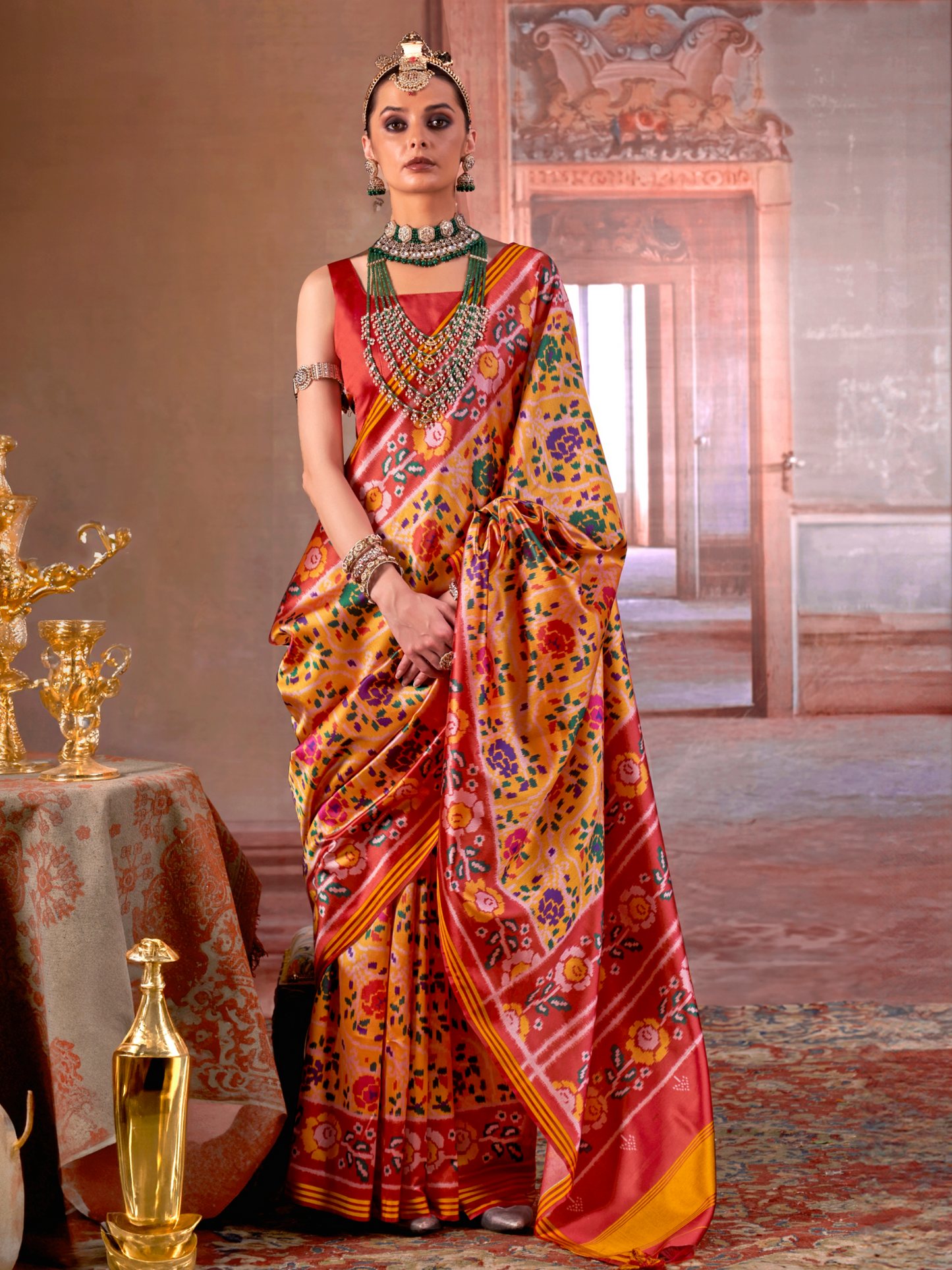 Woman in a colorful saree standing in an ornate room with a table and decorative items.