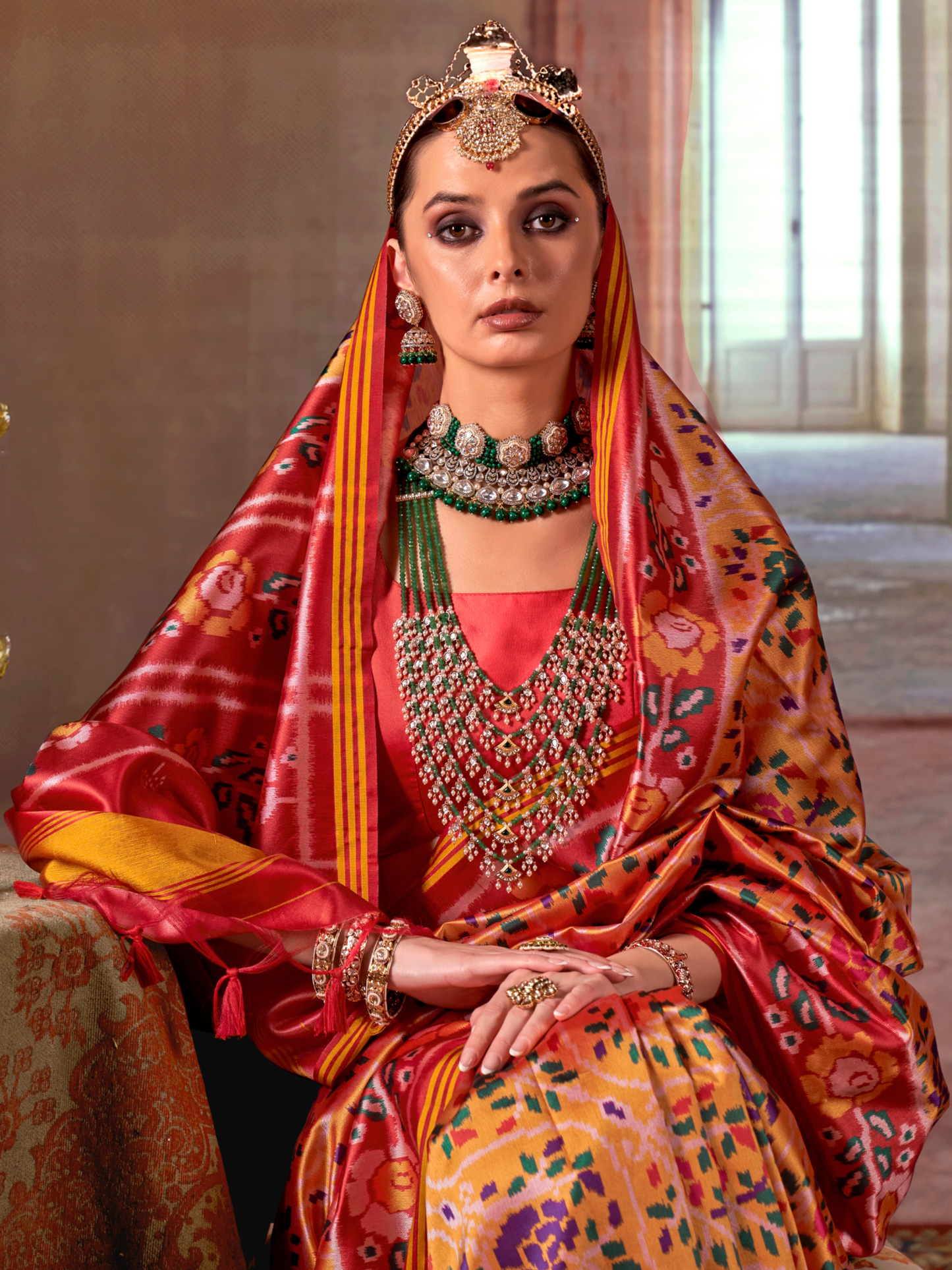 Woman in traditional Indian attire with jewelry, sitting indoors.